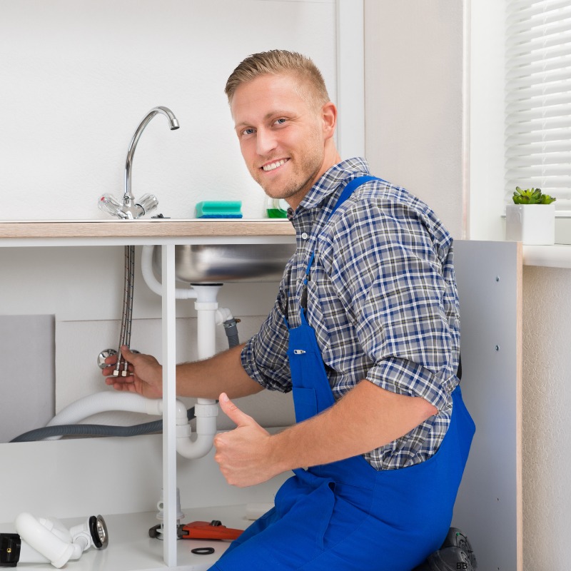 A smiling plumber giving a thumbs up while installing a kitchen sink